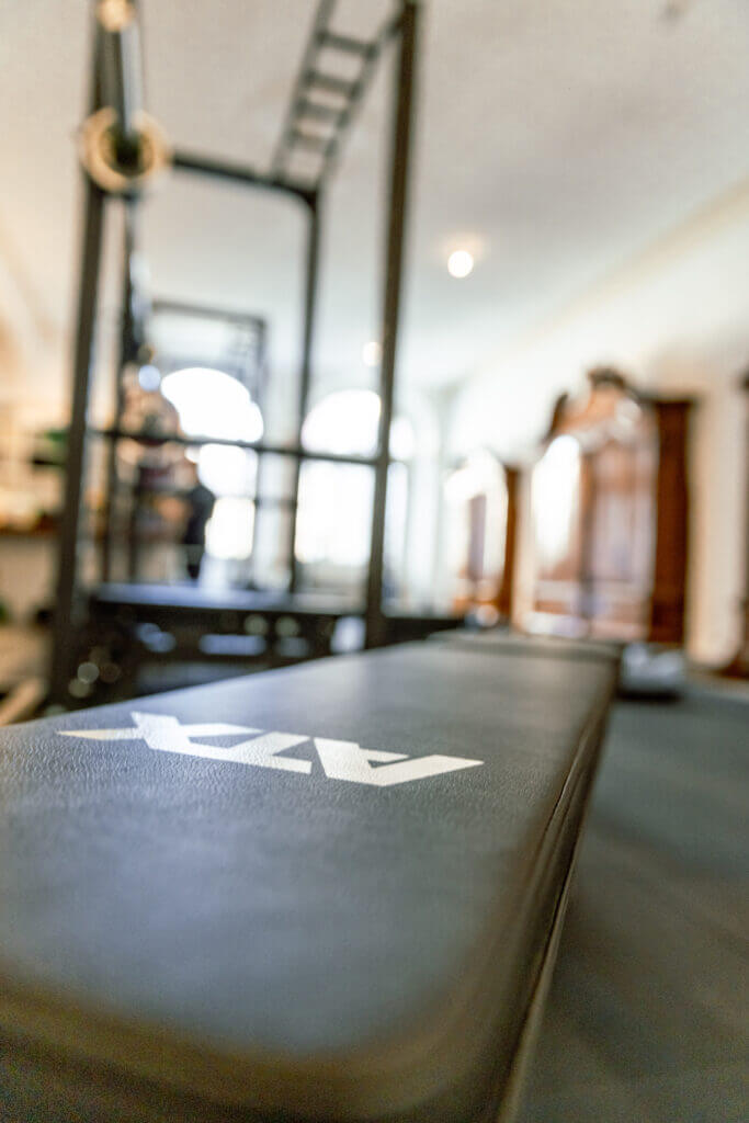 Eine Nahaufnahme einer schwarzen Trainingsbank mit weißem Schriftzug in einem Fitnessstudio mit unscharfen Fitnessgeräten und hellen Fenstern - perfekt für Personal Training in Lübeck.