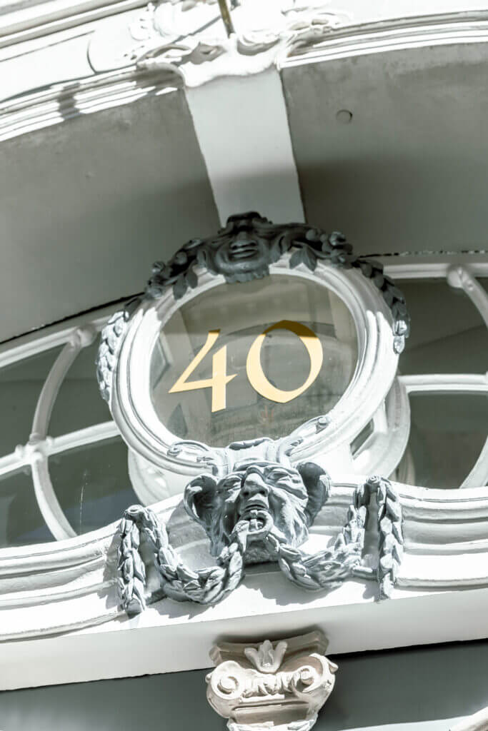 Eine dekorative Gebäudefassade in Lübeck mit der goldenen Zahl 40 in einem verschnörkelten runden Rahmen mit skulptierten Girlanden und einem Gesicht darunter - ein inspirierendes Wahrzeichen in der Nähe der örtlichen Personal Training Studios.