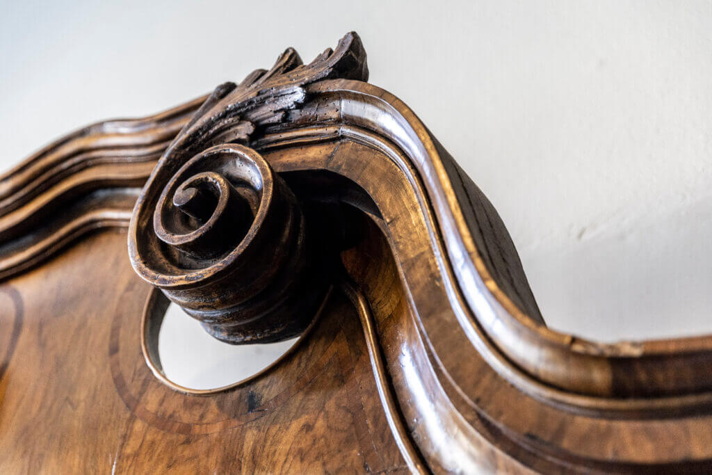 Nahaufnahme eines verzierten, geschnitzten Holzdetails mit einem wirbelnden Muster auf einem antiken Möbelstück in einem Personal Training Studio in Lübeck, mit polierter Holzmaserung und geschwungenen Kanten vor einem hellen Hintergrund.