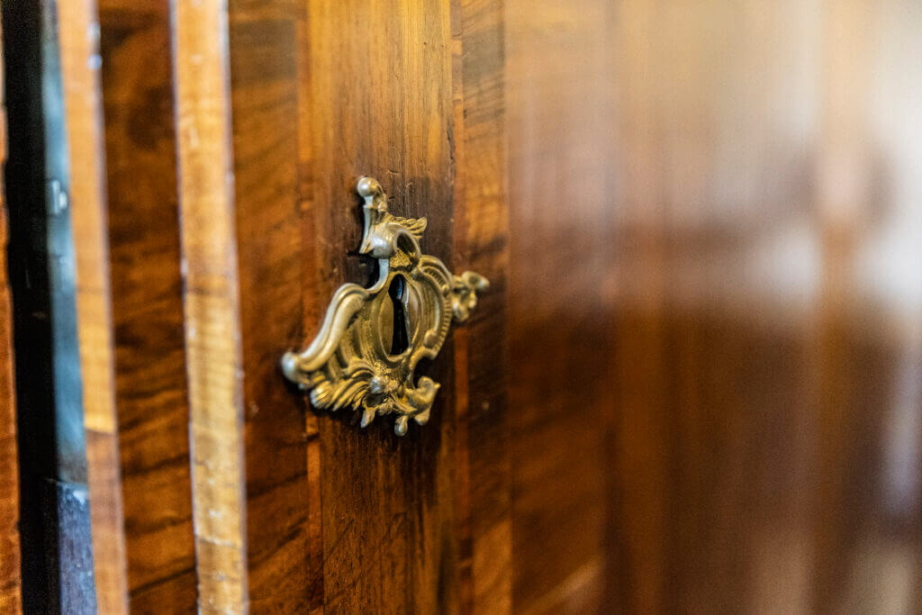 Nahaufnahme eines verschnörkelten Messing-Schlüssellochs auf einer polierten Holzoberfläche, möglicherweise Teil eines antiken Schranks oder einer Tür in einem Personal Training Studio Lübeck. Das Holz hat einen satten, warmen Ton mit sichtbaren Maserungen.